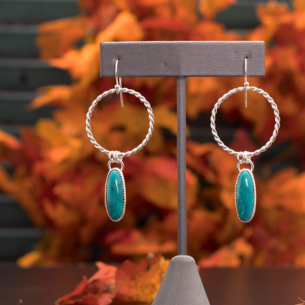 Sterling silver hoop earrings featuring oval turquoise stones on one side and hand-textured silver backs, with front and back of earrings shown on a fall background.