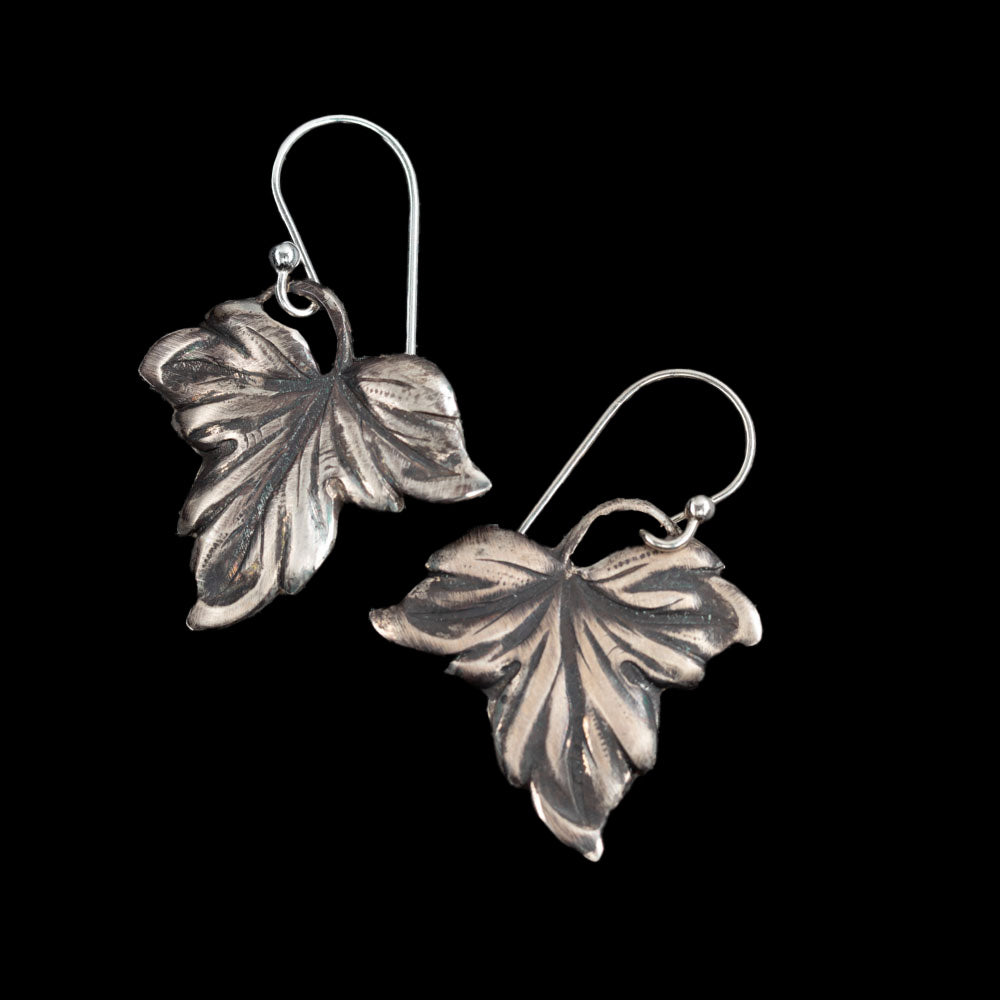 Handcrafted sterling silver drop earrings in a detailed autumn leaf design with oxidized finish, nature-inspired artisan jewelry by Divella Designs – displayed on black background.