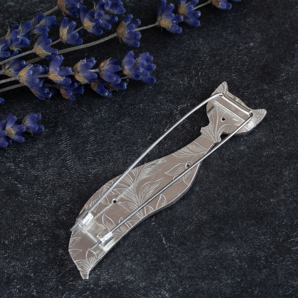 Back of handcrafted sterling silver cat brooch with a minimalist, elongated design and abstract facial features, displayed on a textured black background