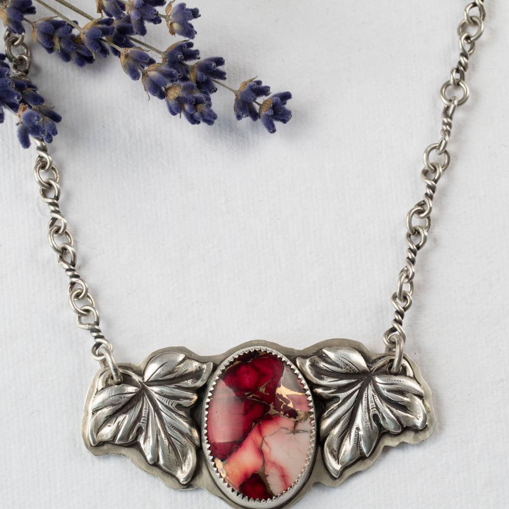 Crimson Bloom necklace with oval dahlia rose stone in pink and red, framed by two detailed sterling silver leaves on a handcrafted silver chain, botanical artisan jewelry.