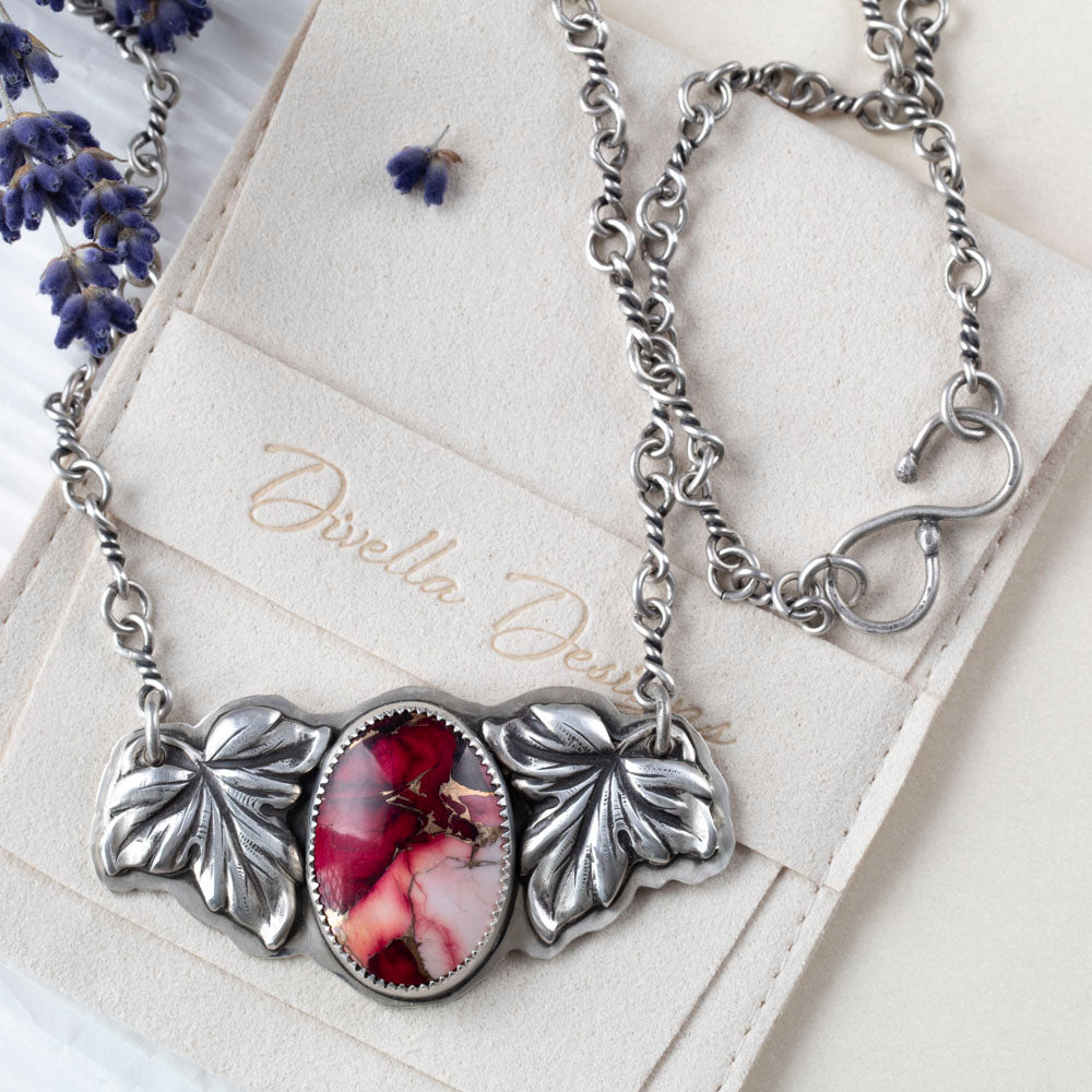 Crimson Bloom necklace with oval dahlia rose stone in pink and red, framed by two detailed sterling silver leaves on a handcrafted silver chain, botanical artisan jewelry.