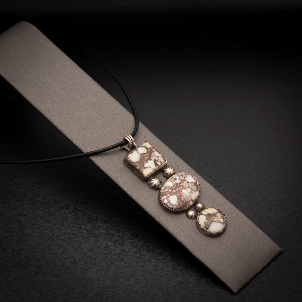 Three-stone Wild Horse pendant with sterling silver accents on a black leather cord, photographed on a neutral display