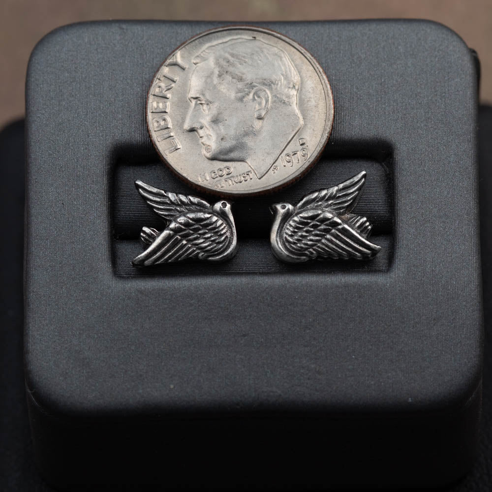 Silver winged earrings on a black display block with a dime for scale.