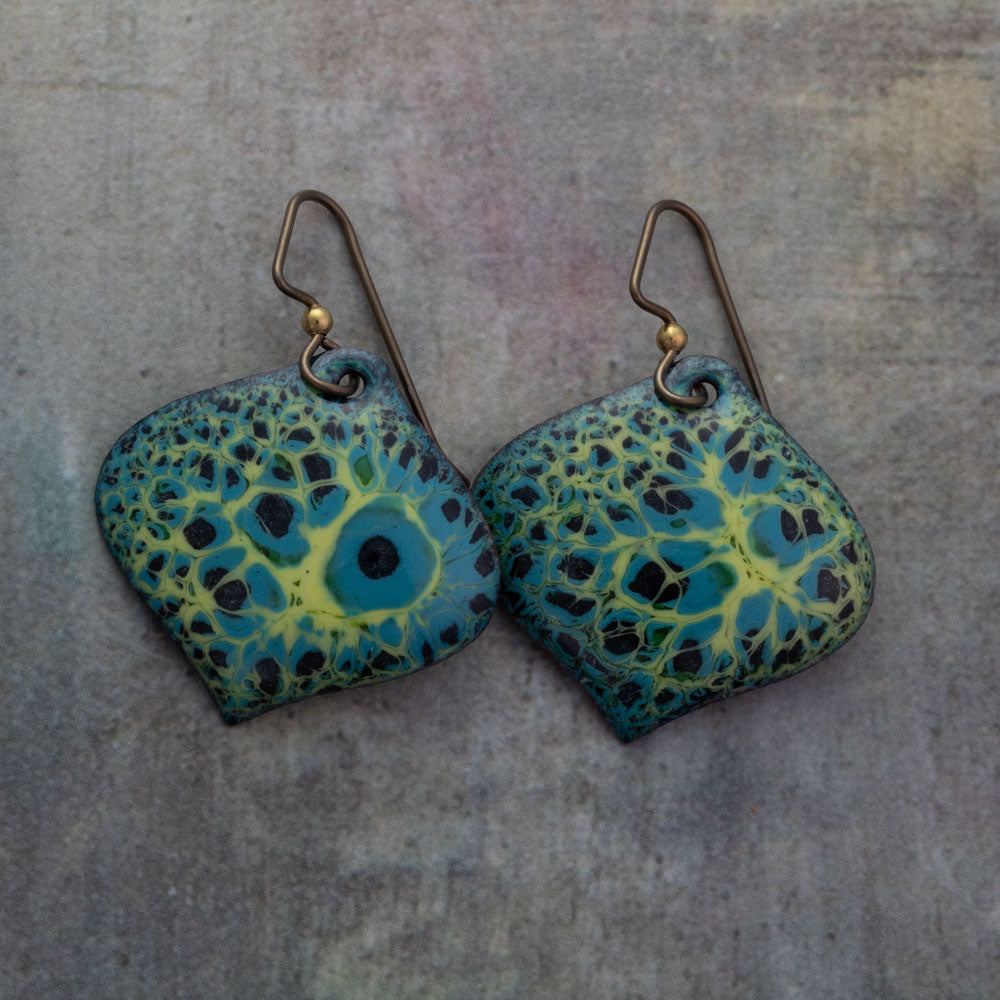 Handcrafted enamel earrings in green, yellow, and blue with lichen-inspired texture and hypoallergenic niobium ear wires, displayed on a stone background.