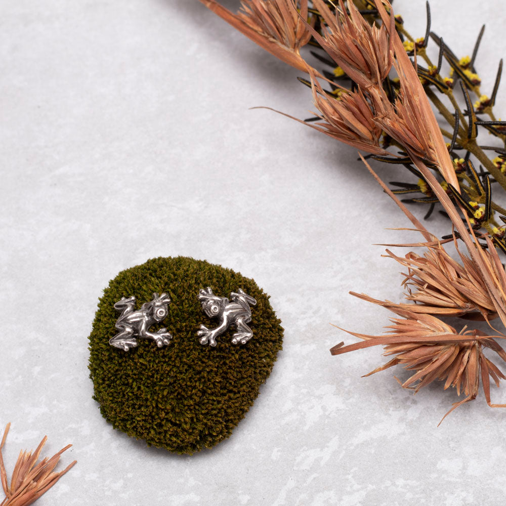 Sterling silver frog stud earrings with playful design, small nature-inspired animal jewelry pictured here on a moss mound with dried flowers.