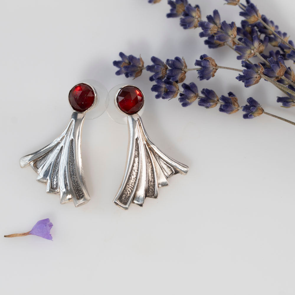 Art Deco-inspired sterling silver earrings featuring deep red faceted garnet stones and flared geometric fan shapes, styled with dried lavender for a vintage botanical vibe