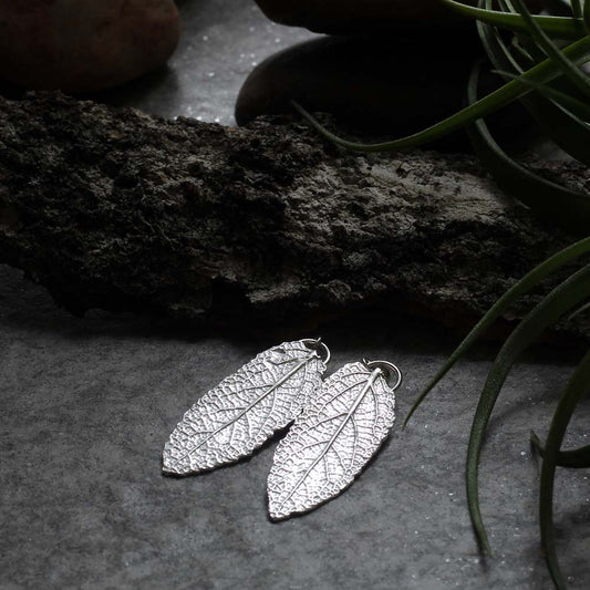 Sterling silver leaf earrings with detailed texture and stud-style dangle design, handmade nature-inspired jewelry.