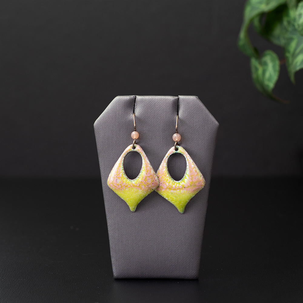 Artisan enamel earrings in pastel pink and vibrant yellow with an organic speckled texture, featuring a diamond-shaped cutout design and niobium ear wires with soft pink stone bead accents.