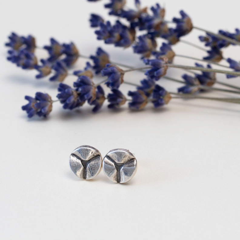 Modern minimalist sterling silver stud earrings with a three-pronged abstract design, displayed on a white background with sprigs of dried lavender.