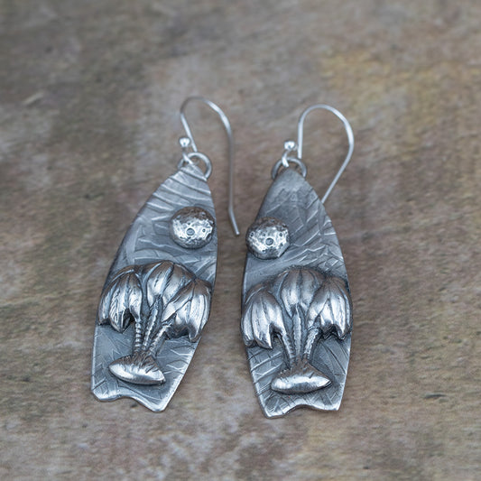 Handcrafted sterling silver earrings featuring sculpted willow trees under a textured full moon on leaf-embossed backdrops – Moonlight Surfing nature-inspired earrings by Divella Designs, shown on earthy background.