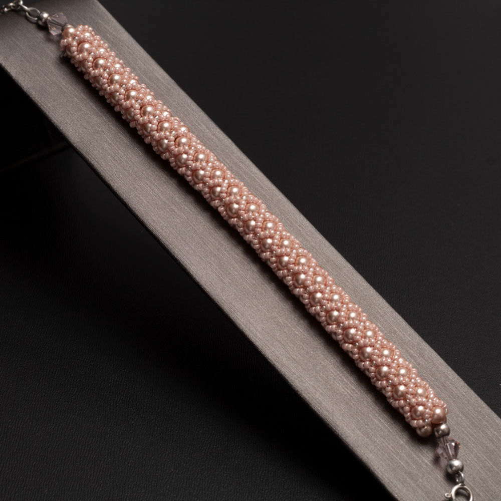 Peach rose beaded bangle bracelet made with Swarovski pearls, displayed on a gray bracelet display.