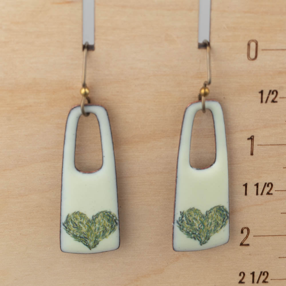 Pair of earrings with heart design on a wooden surface with measurements.