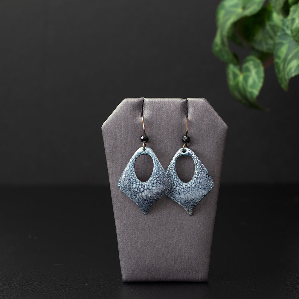 Diamond-shaped enamel earrings with a smoky blue and white speckled pattern, featuring an open teardrop center and niobium ear wires with faceted gemstone beads.