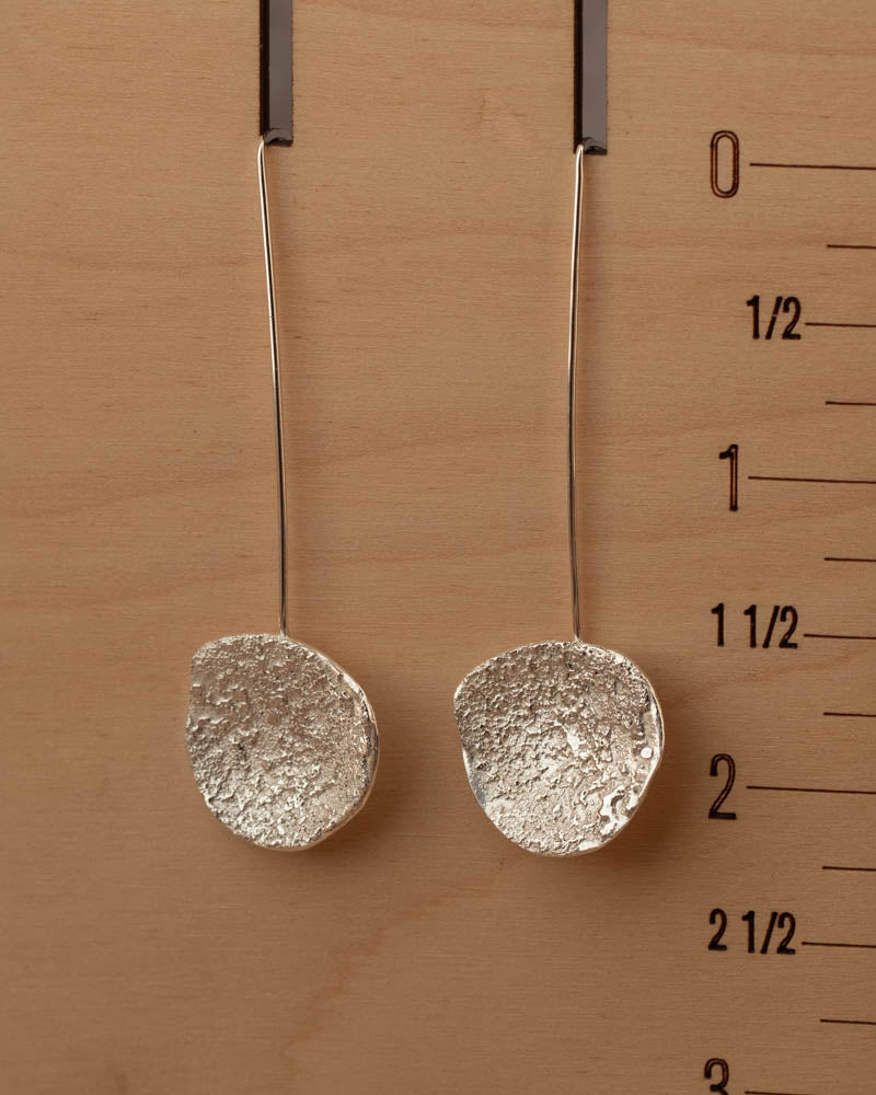 Textured sterling silver dangle earrings resting on rustic wood, showcasing handmade craftsmanship by Divella Designs Jewelry.