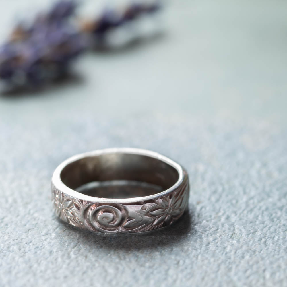 Sterling silver floral band ring with scroll texture on soft blue background