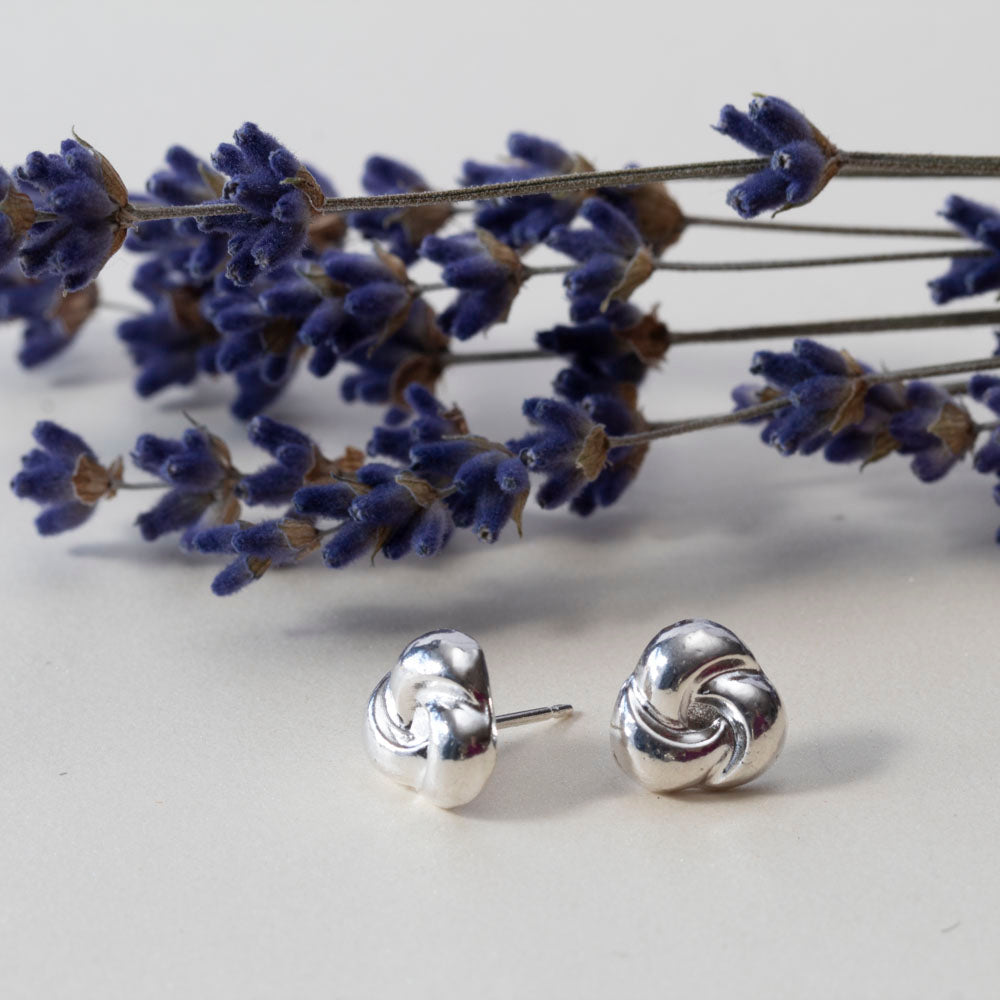 Sterling silver knot stud earrings displayed in front of dried lavender on a light surface.