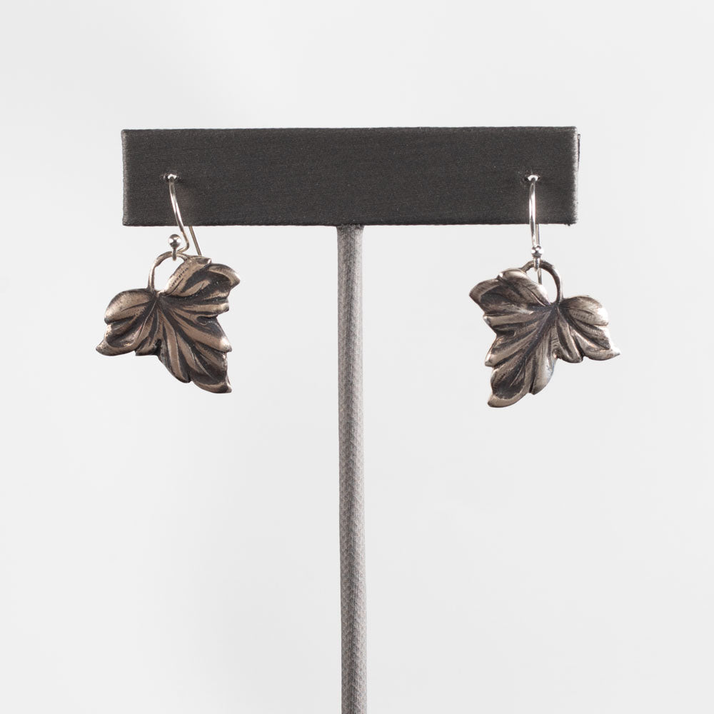 Handcrafted sterling silver drop earrings in a detailed autumn leaf design with oxidized finish, nature-inspired artisan jewelry by Divella Designs – displayed on white background.