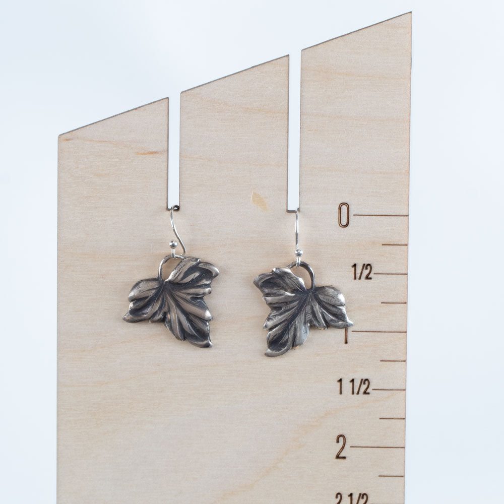 Handcrafted sterling silver drop earrings in a detailed autumn leaf design with oxidized finish, nature-inspired artisan jewelry by Divella Designs – displayed on wood ruler for scale.