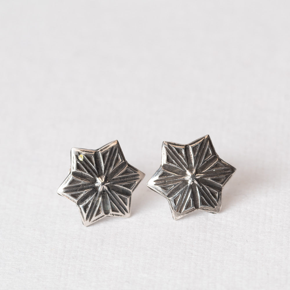 Pair of handcrafted sterling silver star-shaped stud earrings with etched radiating lines, displayed on a light fabric backgroun