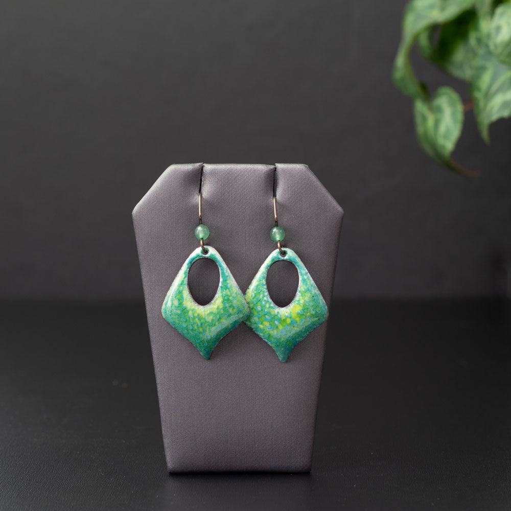 Handcrafted green enamel earrings with hints of yellow and blue in a diamond-shaped cutout design, paired with niobium ear wires and green stone bead accents, inspired by fresh spring meadows.