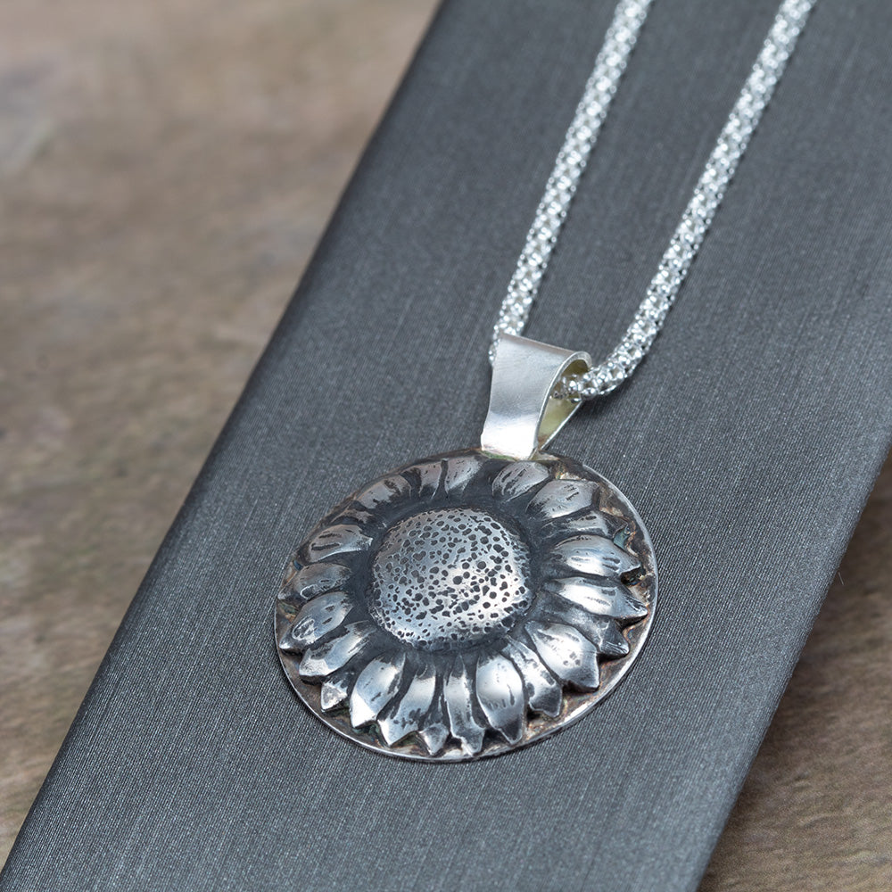 Handcrafted sterling silver sunflower pendant with oxidized details for depth and texture, hanging on a shimmering chain – artisan floral necklace by Divella Designs