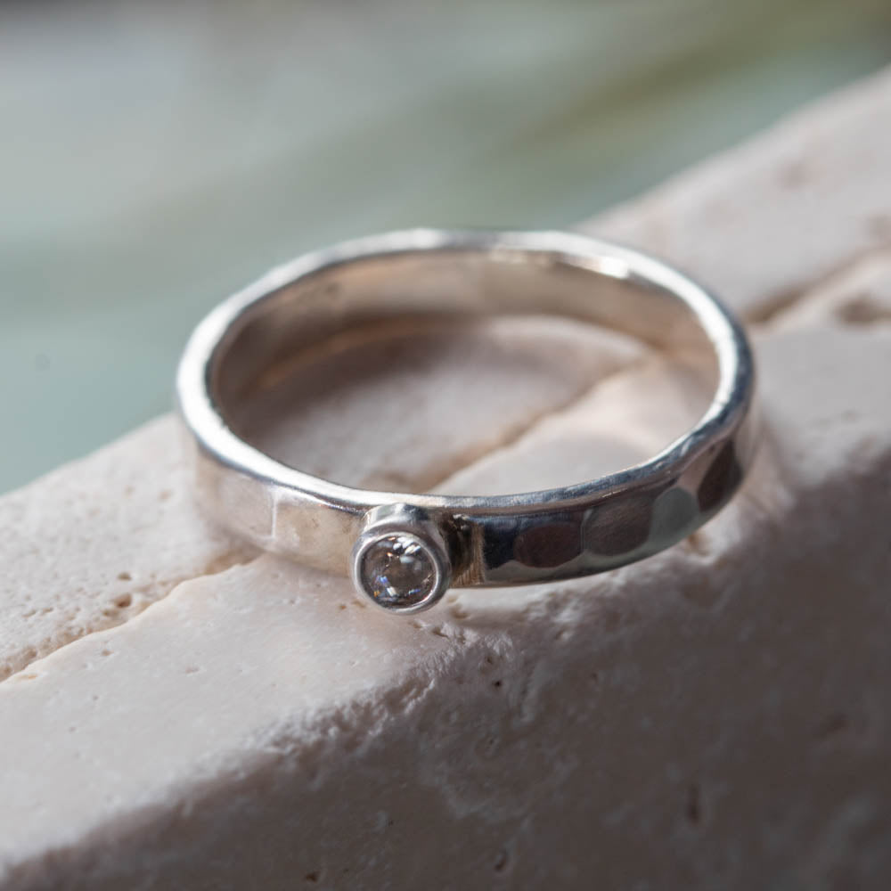 Sterling silver hammered band ring with tube-set cubic zirconia on neutral stone background