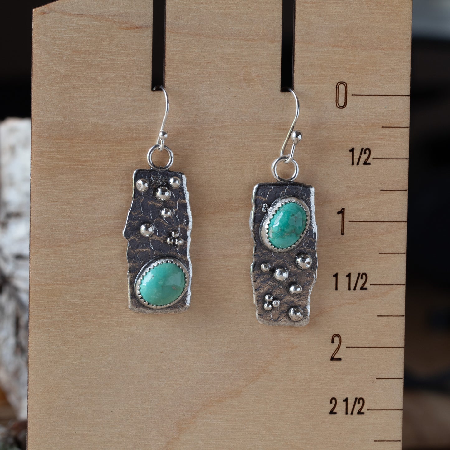 Pair of silver earrings with turquoise stones on a wooden ruler for scale.