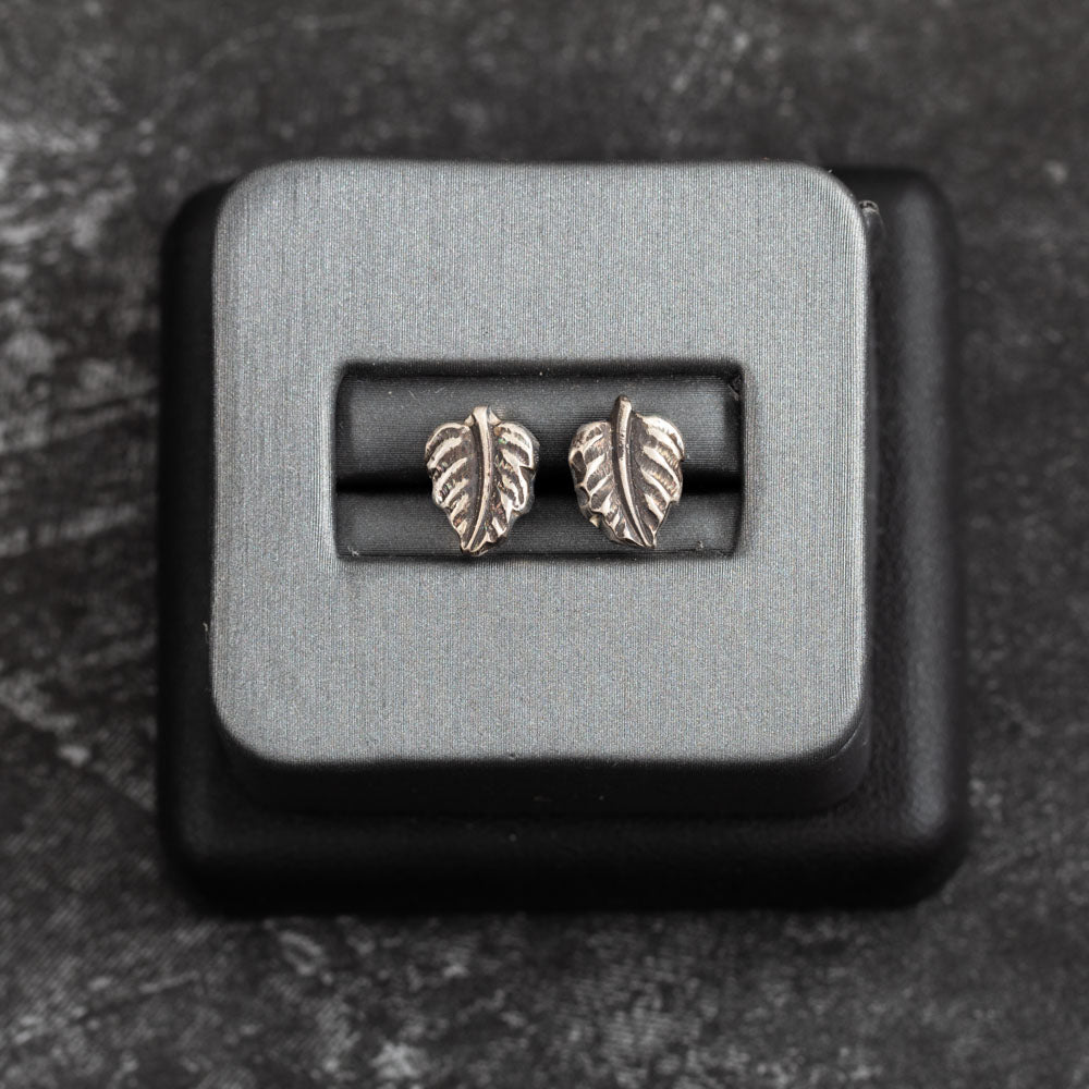 Tiny sterling silver leaf stud earrings with delicate vein detailing, nature-inspired minimalist design displayed in a jewelry box – handmade by Divella Designs.