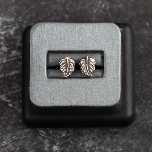 Tiny sterling silver leaf stud earrings with delicate vein detailing, nature-inspired minimalist design displayed in a jewelry box – handmade by Divella Designs.