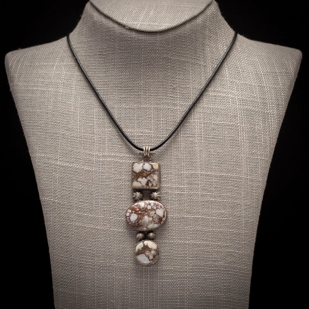 Three-stone Wild Horse pendant with sterling silver accents on a black leather cord, photographed on a neutral display.