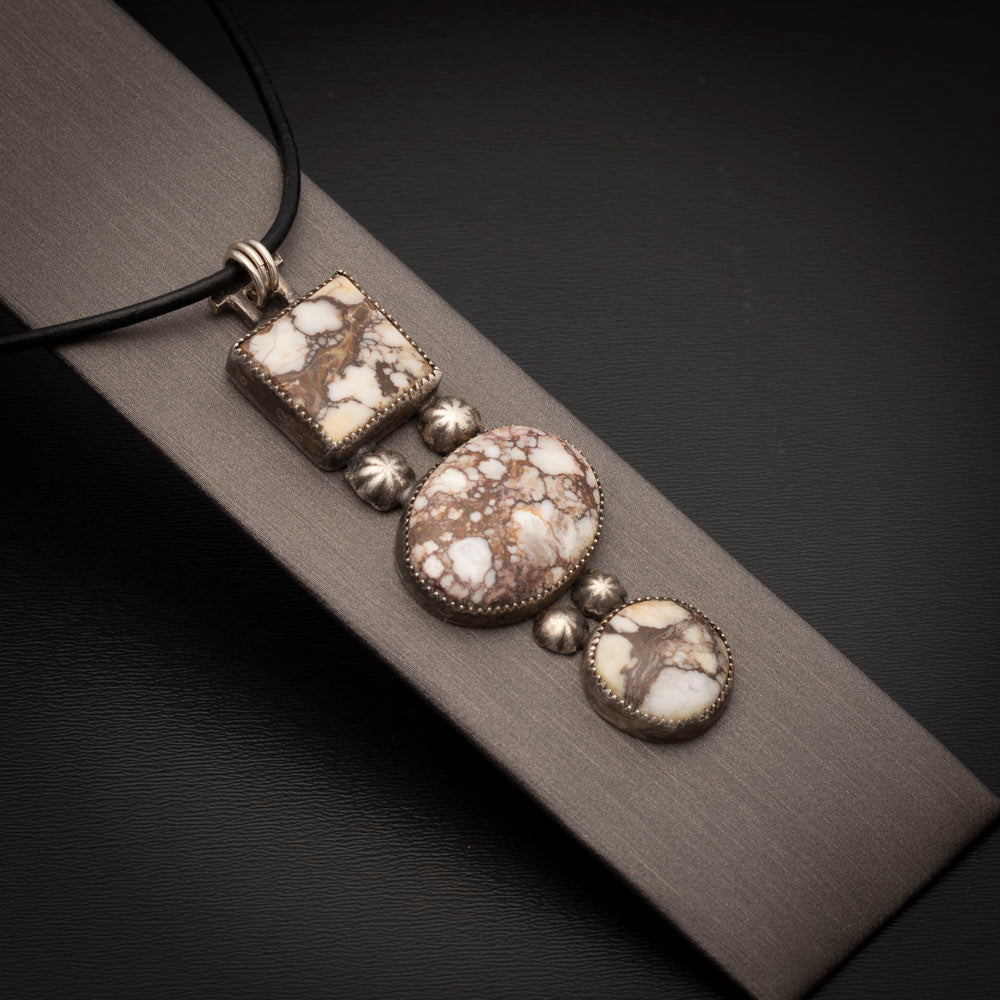 Three-stone Wild Horse pendant with sterling silver accents on a black leather cord, photographed on a neutral display.