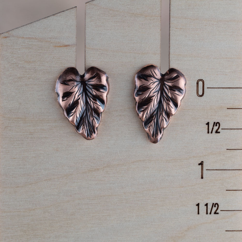 handmade copper leaf earrings with sterling silver posts pictured on a wooden ruler for scale. Nature-inspired artisan botanical jewelry