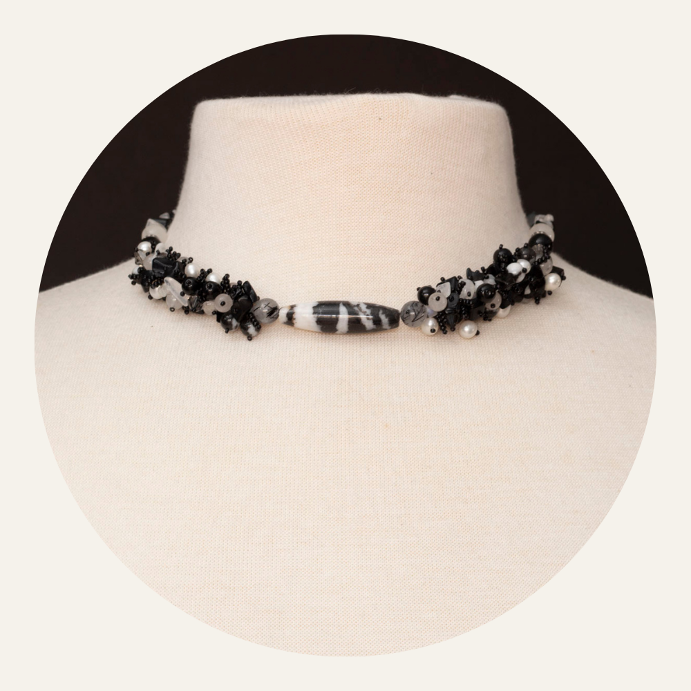 Black and white gemstone necklace featuring zebra jasper, clear quartz, and freshwater pearls in a clustered design, displayed on a neutral linen mannequin.