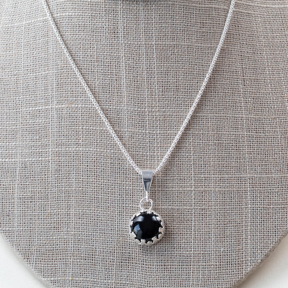 Sterling silver pendant necklace featuring a round black onyx stone in a scalloped bezel setting, displayed on a gray bust.