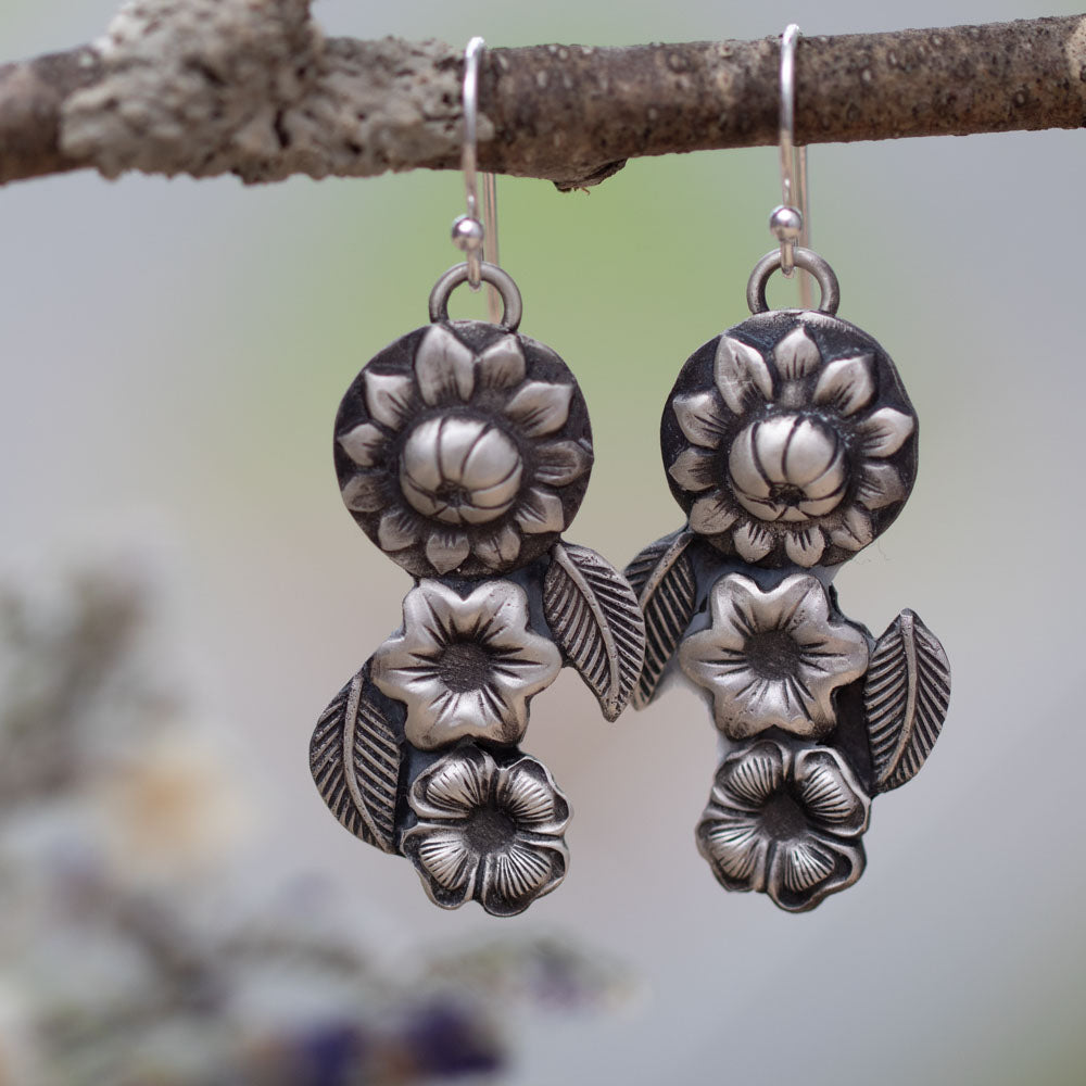 Handmade sterling silver flower earrings with botanical leaf design against a light background.