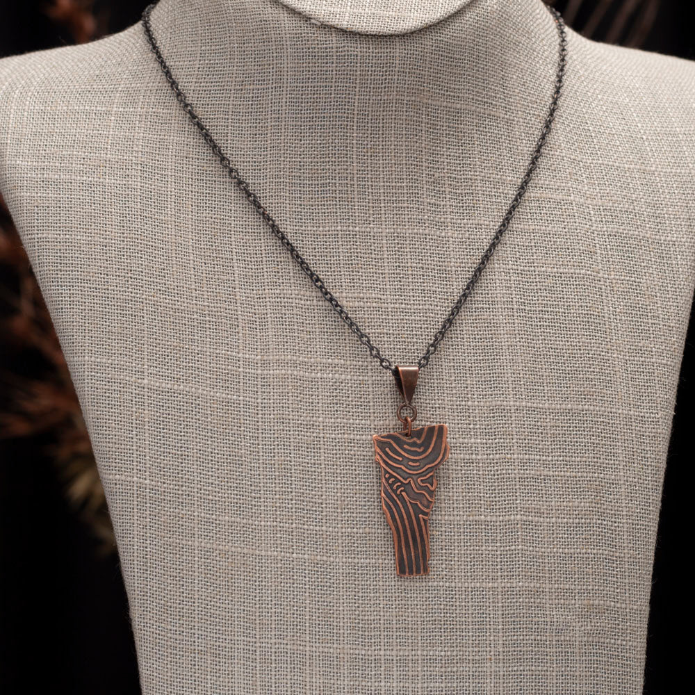 Copper pendant featuring a wood grain texture styled on a neutral bust.