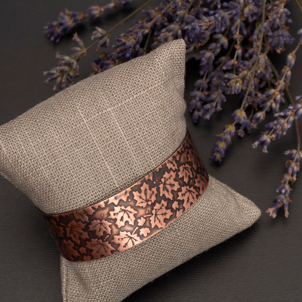 Copper etched maple leaf cuff pictured an a jewelry pillow with a gray background and lilac sprigs.