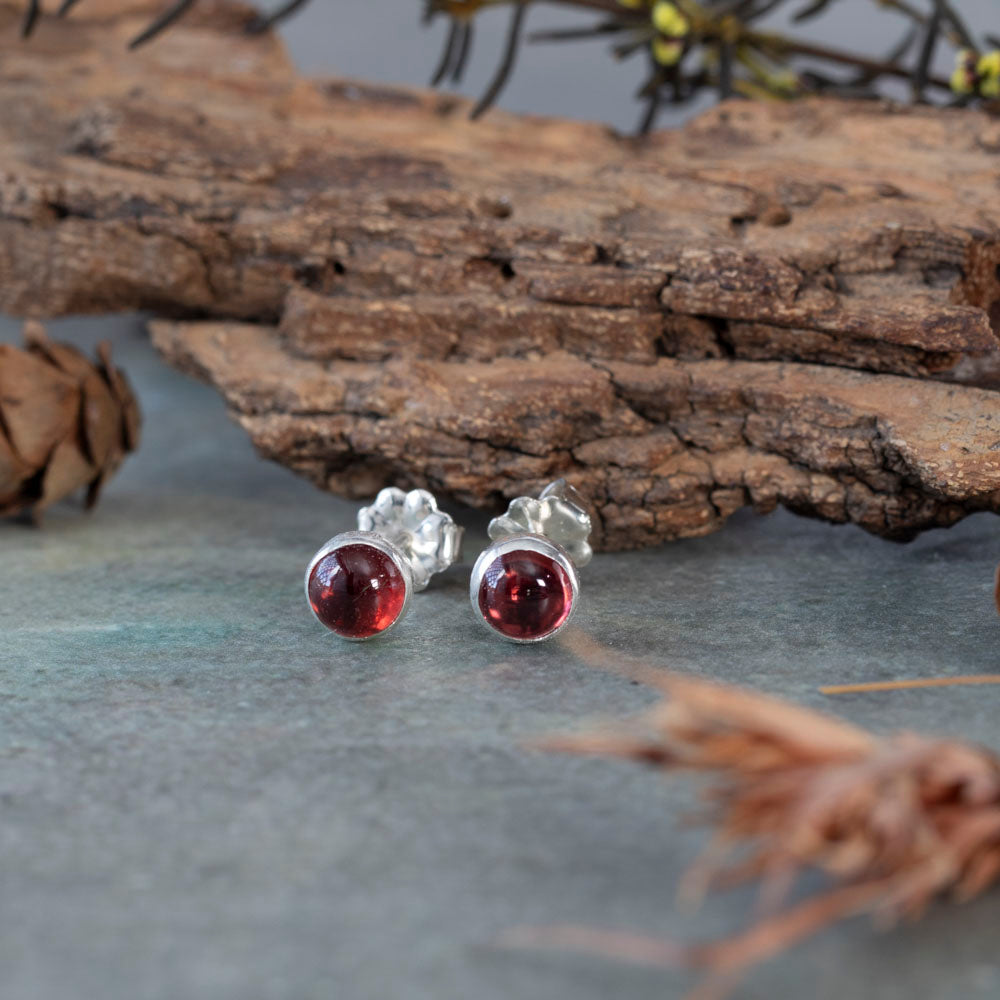 Round garnet stud earrings in sterling silver settings, photographed on slate with wood accents.
