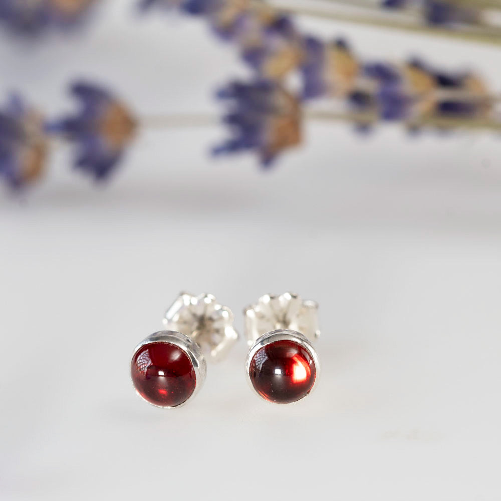 Round garnet stud earrings in sterling silver settings, styled with dried lavender on a white background.