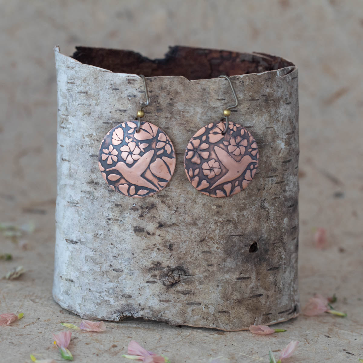 Handmade copper hummingbird earrings with floral motif, featuring etched round disc design and oxidized finish for a rustic, nature-inspired artisan look.