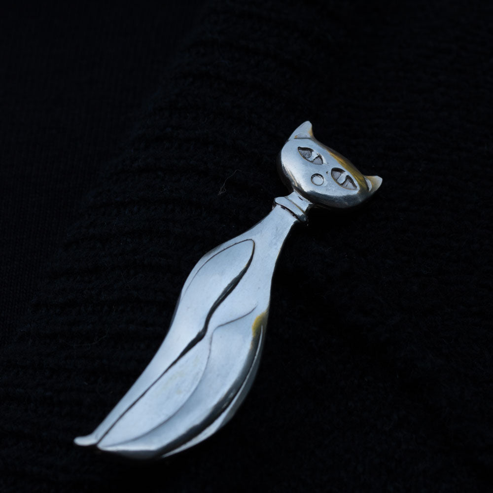 Handcrafted sterling silver cat brooch with a minimalist, elongated design and abstract facial features, displayed on a black background.