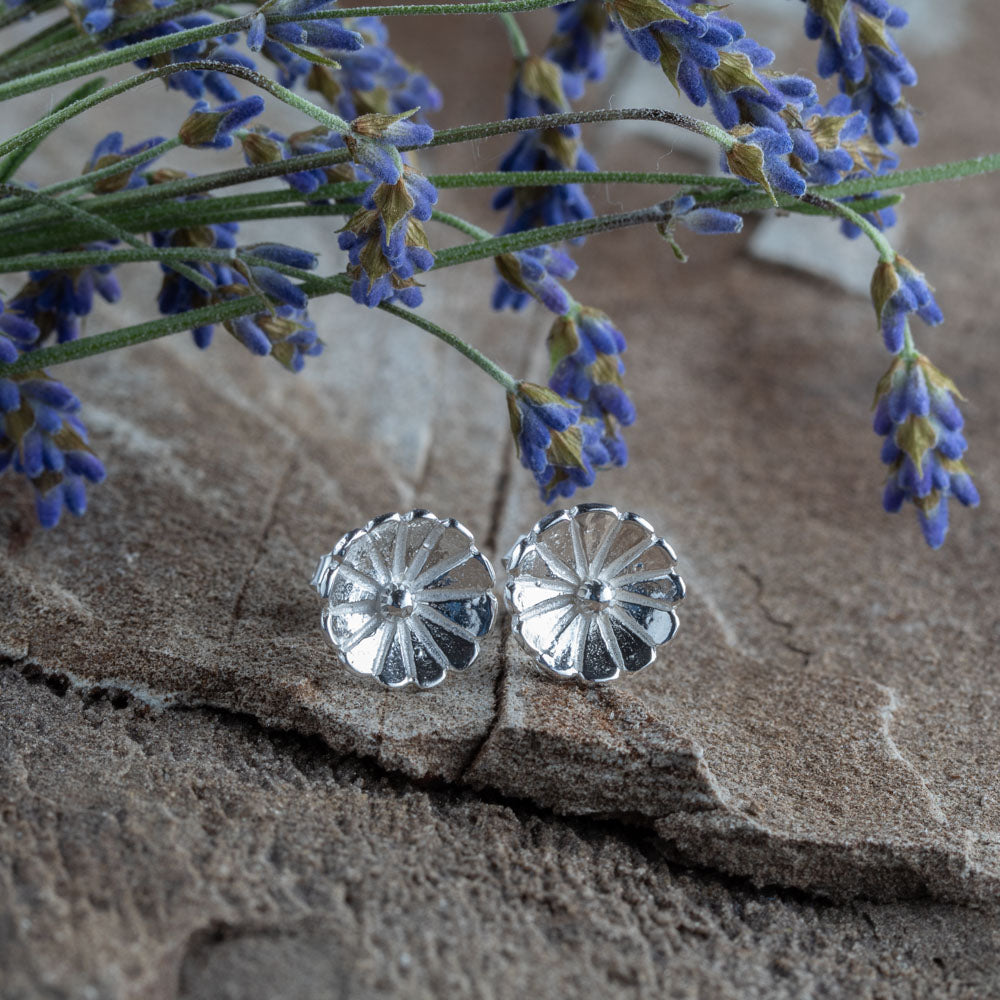 Sterling silver flower stud earrings – small hand-crafted floral design with petal texture, polished finish, perfect for everyday wear. Displayed on natural stone with lavender sprigs.