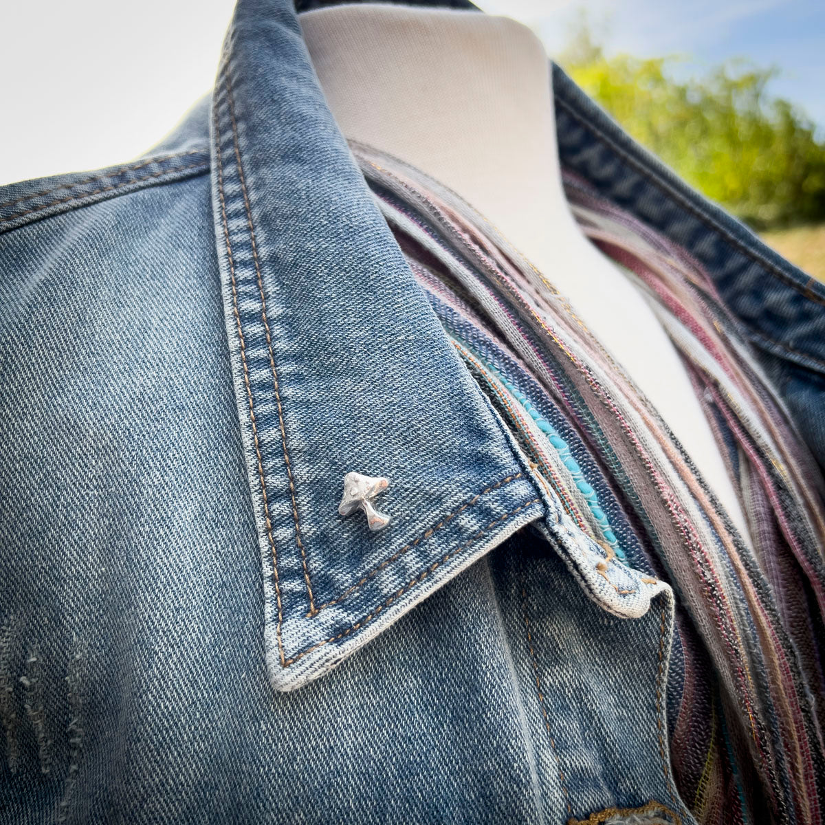 Close-up of a denim jacket on a mannequin with a blurred outdoor background