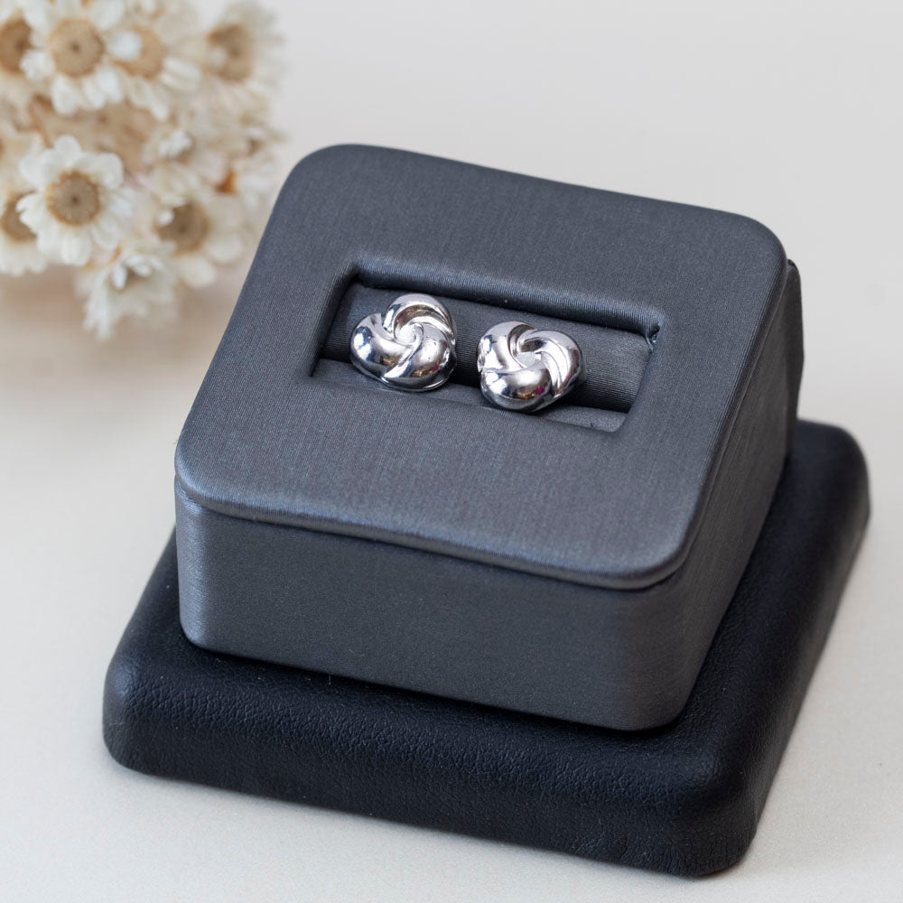 Sterling silver knot stud earrings displayed in a jewelry box in front of dried lavender on a light surface.