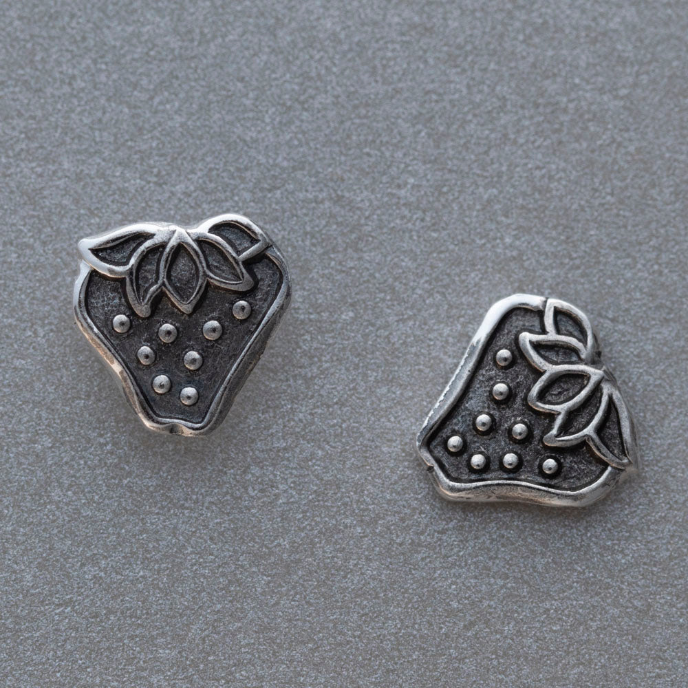 Close up of handcrafted silver strawberry stud earrings with leafy detail and dotted texture, featuring whimsical fruit-inspired design and rustic botanical charm.