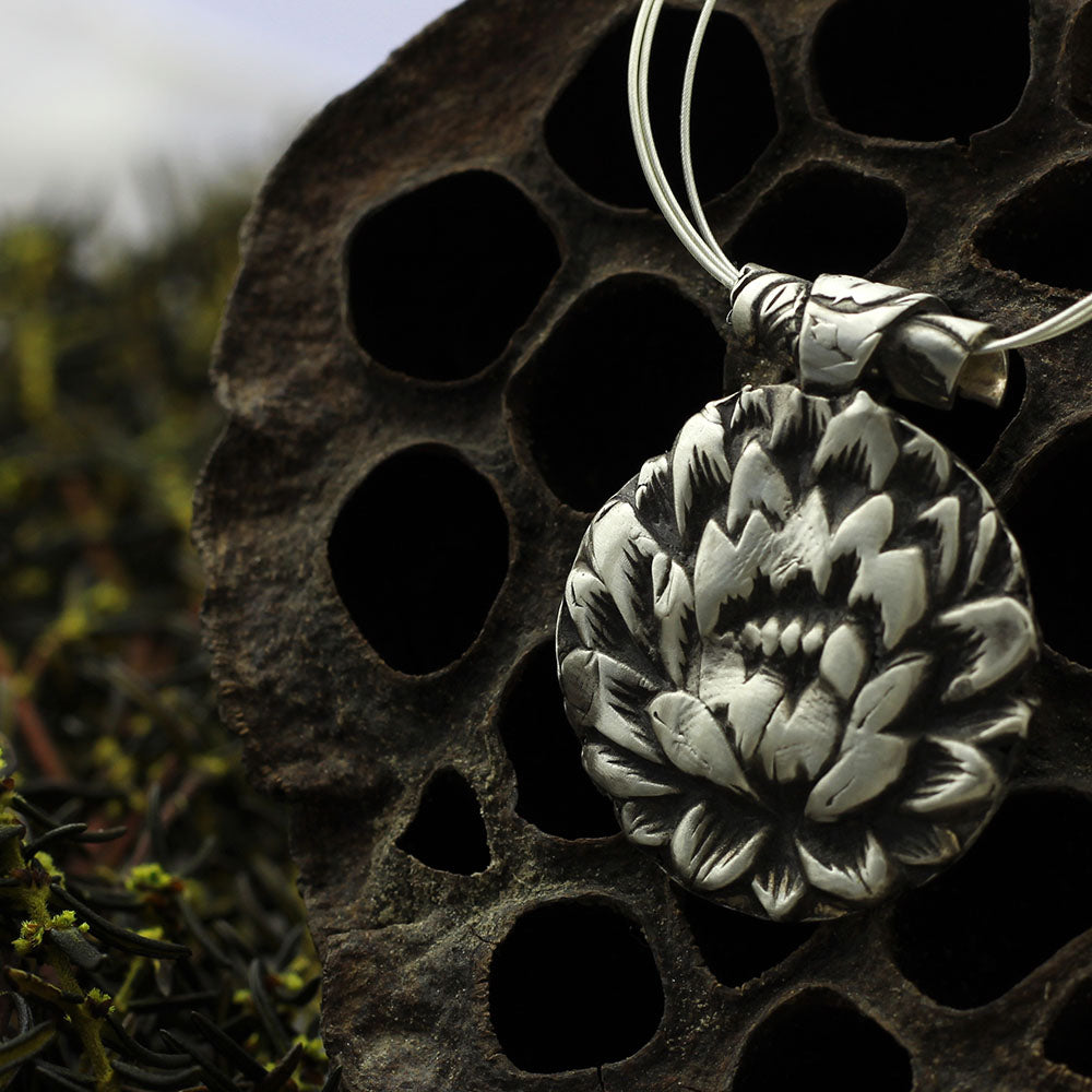 Close up view of the lotus flower pendant on triple-strand sterling AccuFlex wire necklace.