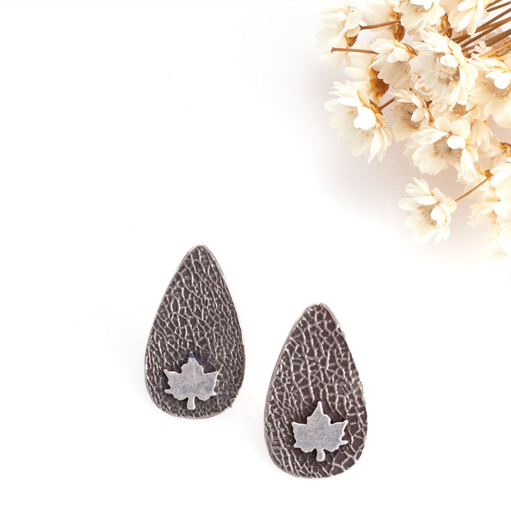 Sterling silver teardrop stud earrings with textured finish and small maple leaf detail, ⅞ inch long
