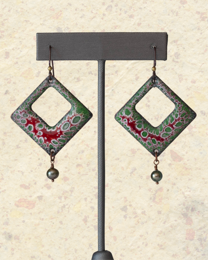 Handcrafted enamel earrings with red and green organic cell pattern, diamond shape with freshwater pearl dangles – Forest Cell design by Divella Designs, hangin vertically with a stone background.