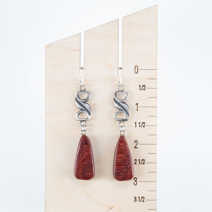 Handcrafted dangle earrings with deep red Bibingka wood teardrops and sculptural sterling silver links, modern artisan design displayed on wooden ruler for scale – by Divella Designs