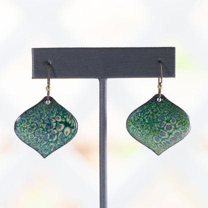 Handmade enamel earrings in green, yellow, and purple with lichen-inspired texture, diamond shape, and antique brass ear wires on a stone background.